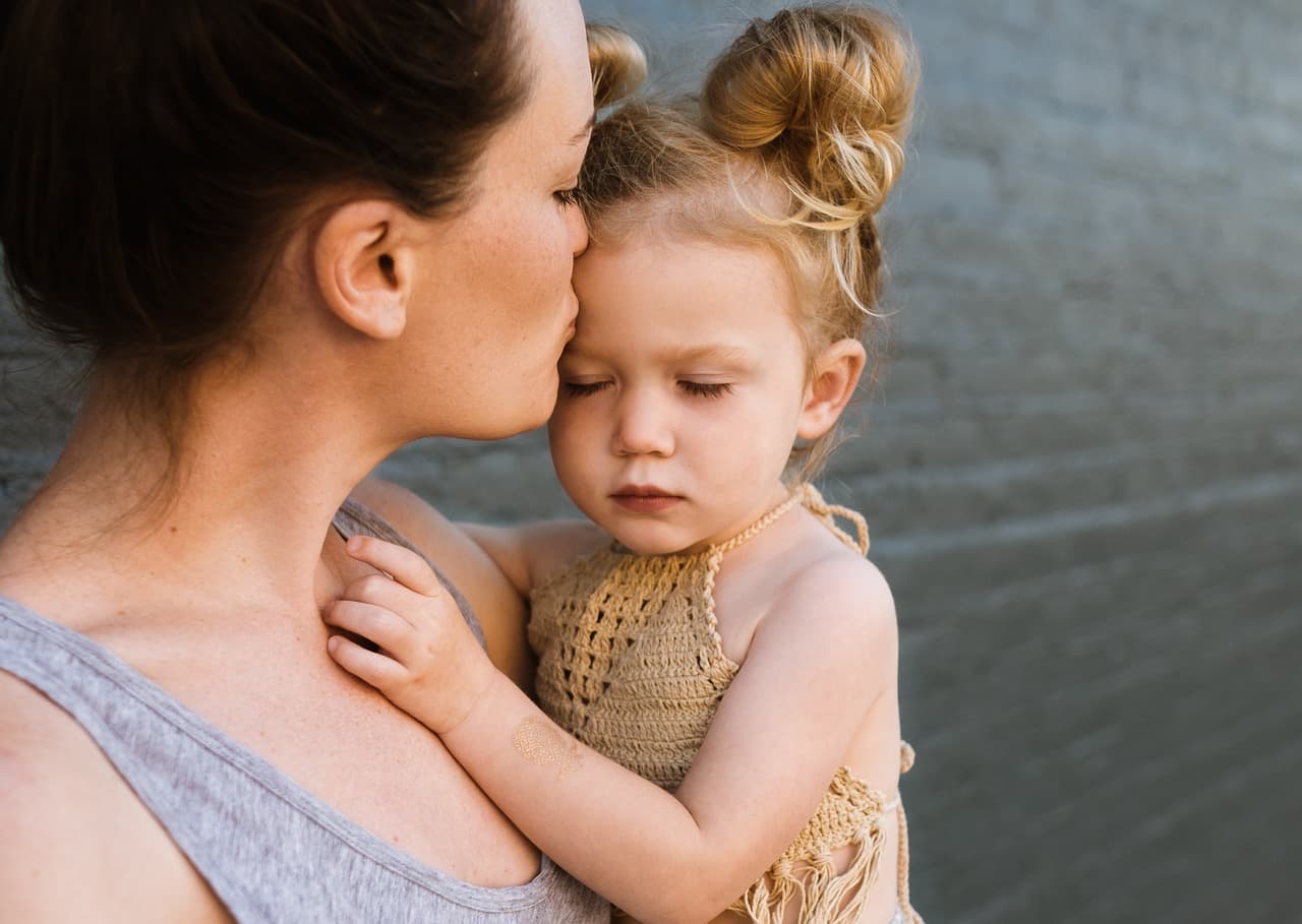 Parent using a fine-toothed nit comb on a child's hair near a bright window, checking for head lice