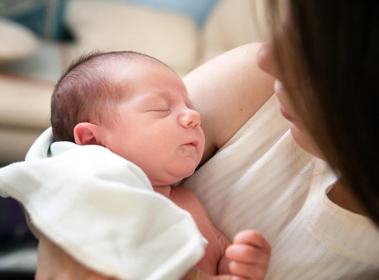 Parent holding an infant upright against their shoulder after feeding in a cozy nursery setting