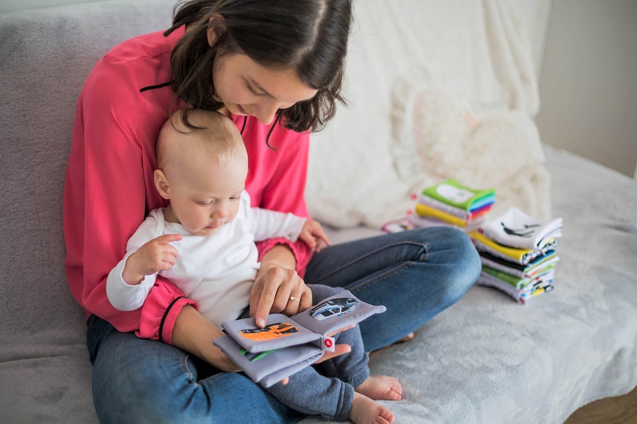 Mother reading a picture book with her toddler on her lap, pointing at pages, warm home setting